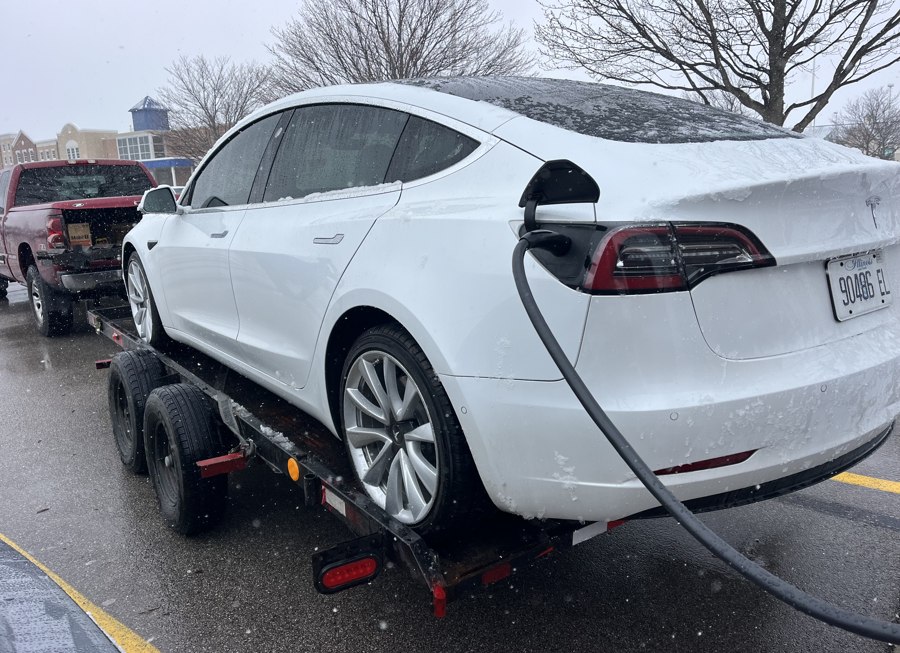 Towing Truck Transporting a Tesla Electric Car to a Charging Station A professional towing truck carefully towing a disabled Tesla Model 3 to an EV charging station for emergency power.
